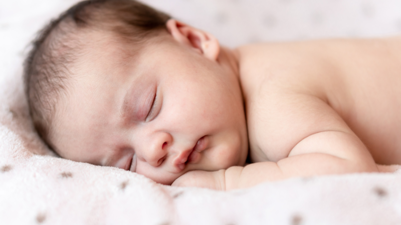Bé sơ sinh nằm úp trên khăn mỏng an toàn dưới sự quan sát của cha mẹ