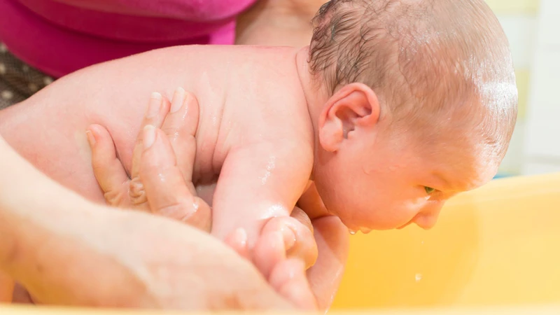 Đỡ ngực bé lên cánh tay để dễ dàng làm sạch vùng lưng và mông